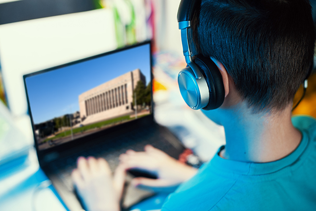 Lapsi katsoo tietokoneelta kuulokkeet päässä kuvaa Eduskuntatalosta.
